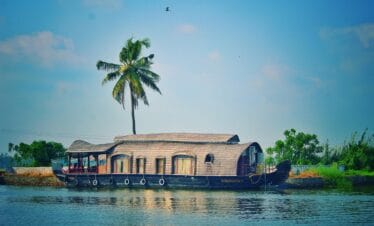 Picturesque view of river with green palms on bank and shabby wooden boathouse under blue sky in tropical countryside